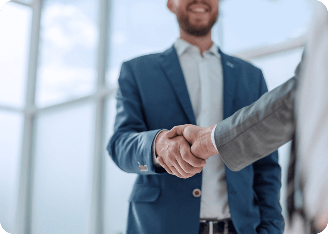 Two man shaking hands in front of a window, exemplifying continuous improvement and empowering individuals to achieve meeting objectives.