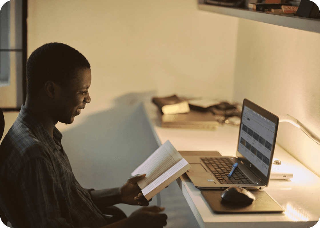 A man sitting at a desk with a laptop and a book, getting Spiky Academy's comprehensive statistical analysis tips and data-driven insights.