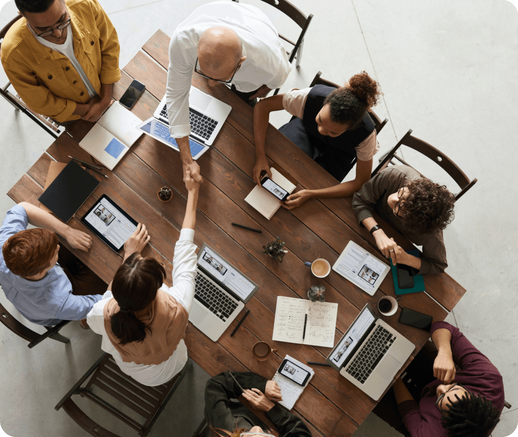 People huddled around a table, working on laptops and discussing Spiky's AI tool streamlining customer success tasks for effortless wins.