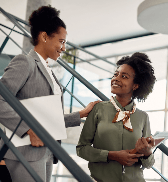 Two professional businesswomen are conversing about Spiky vs. Fireflies methodology and discussing revenue intelligence on office stairs.