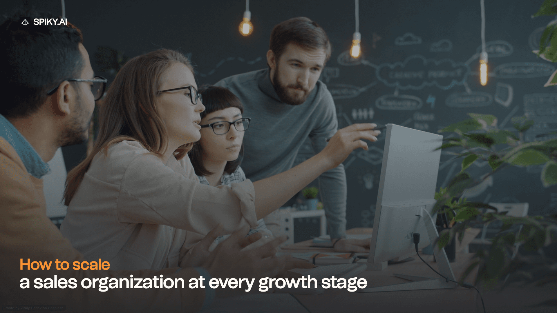 A diverse sales team collaborates around a desktop computer in a modern office, with chalkboard sketches and text about scaling growth.