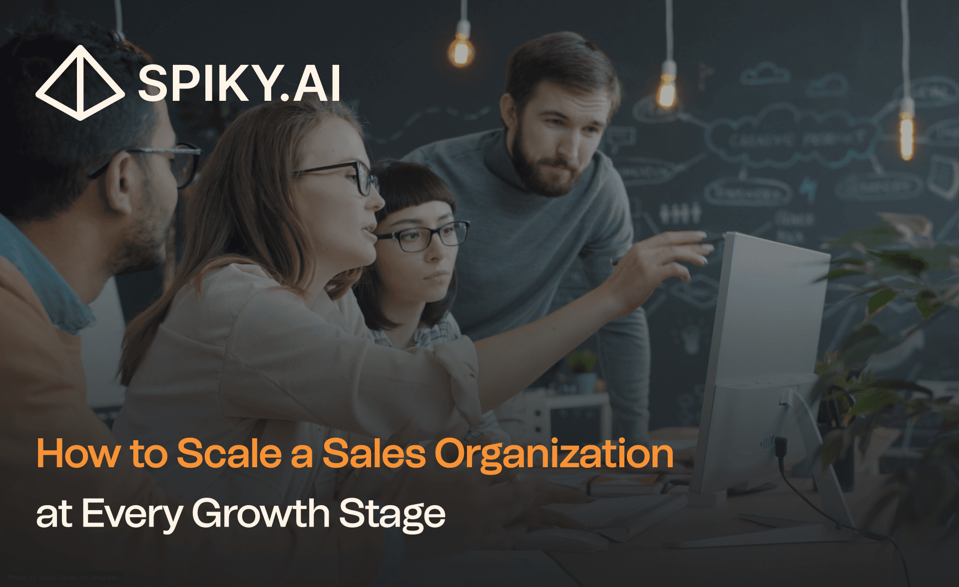 A diverse sales team collaborates around a desktop computer in a modern office, with chalkboard sketches and text about scaling growth.