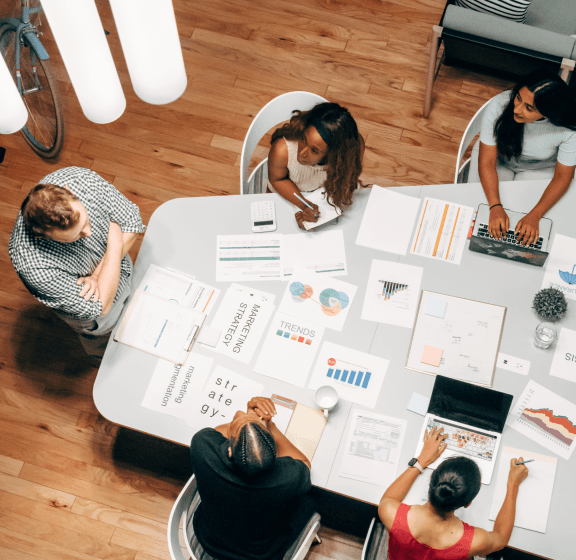 Individuals gathered around a table, engaged in paper-based discussions, emphasizing communication for customized solutions and optimal returns.