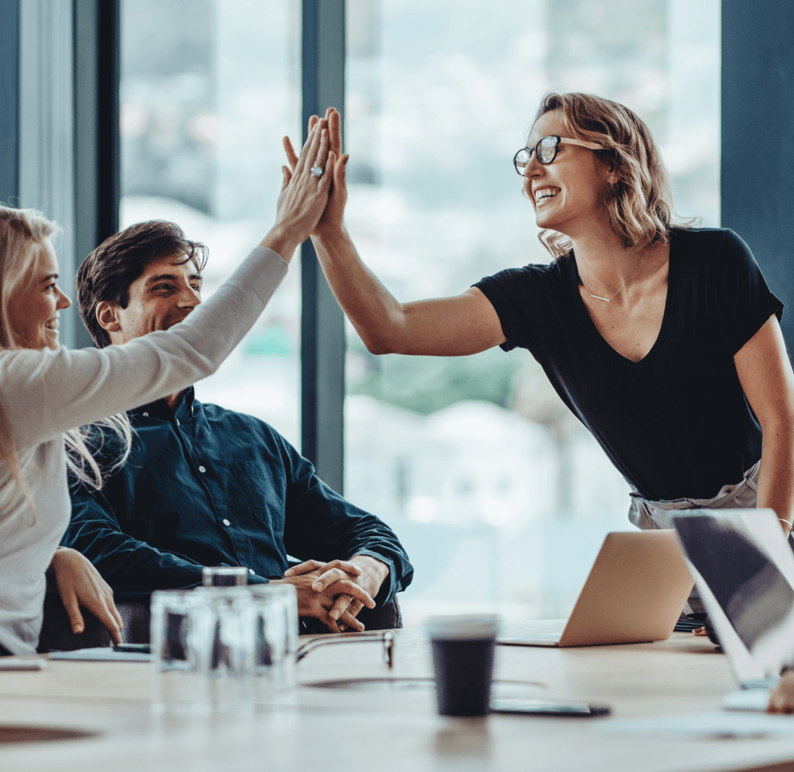 A group of people enthusiastically high-fiving each other in a meeting, showcasing a client-centric approach and tangible results.